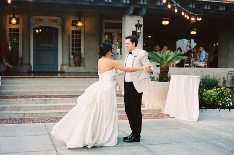A bride and groom sharing a first dance outdoors, the groom in a tailored tan tuxedo jacket