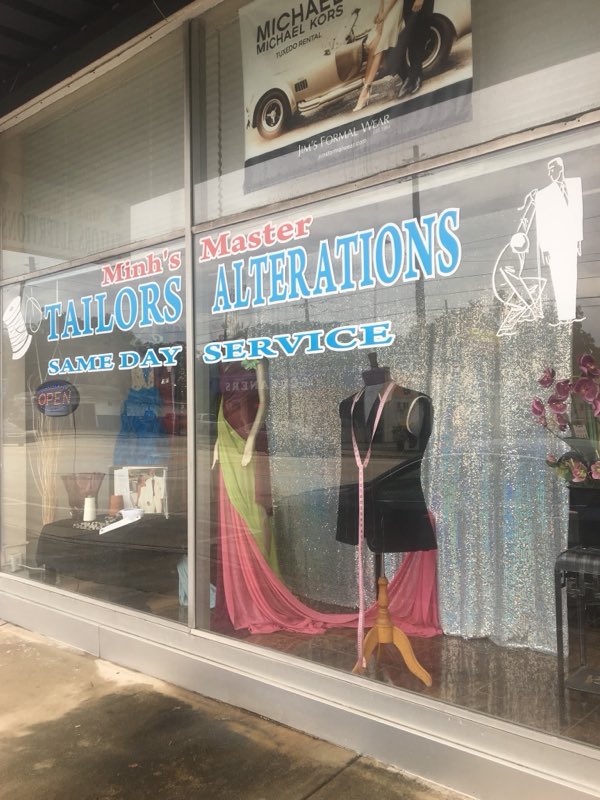 Minh's shop window lettered Tailors, Alterations, Same Day Service with a suit form and gowns on display