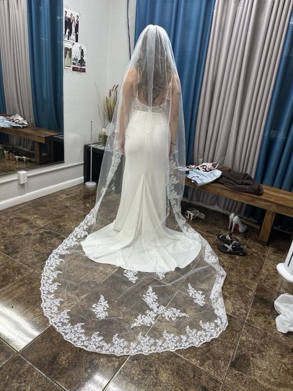 A bride from behind wearing a fitted gown with a long lace cathedral veil trailing on the floor