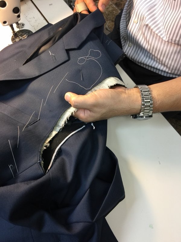 Hand-tailoring a navy suit jacket with basting stitches at the sewing machine